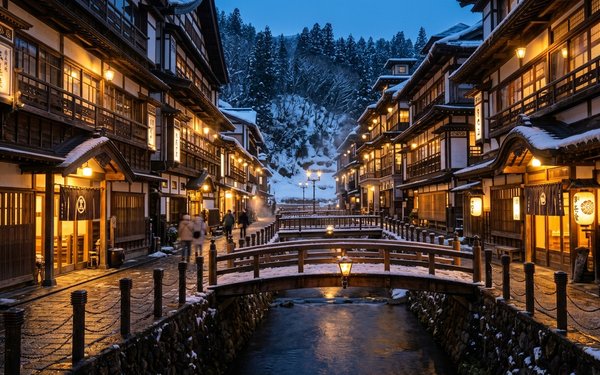 Snow-covered wooden ryokan inns line a canal at Ginzan Onsen, their warm lanterns glowing over bridges at dusk.